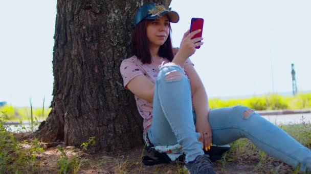 Mujer Joven Descansa Con Teléfono Móvil Sentado Cerca Del Árbol — Vídeos de Stock