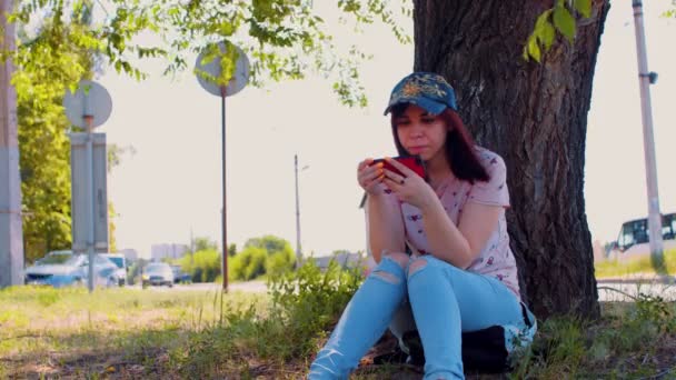 Mujer Joven Descansa Con Teléfono Móvil Sentado Cerca Del Árbol — Vídeo de stock