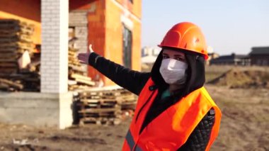 Female engineer in the construction helmet and antiviral protective mask inspects a building or object reconstruction. 