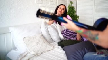 Bir adam yatak odasında güzel bir kadına gitar çalar. Aşık mutlu bir çift. Genç şık moda çiftimizin göz kamaştırıcı şehvetli portresi. Genç adam sevgili kızı için gitar çalıyor..