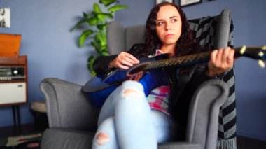 Gündelik giysiler içinde genç ve güzel bir kadın koltuğunda oturup gitar çalıyor. Müzik aletleriyle tek başına dinlenen güzel bir kadının portresi..
