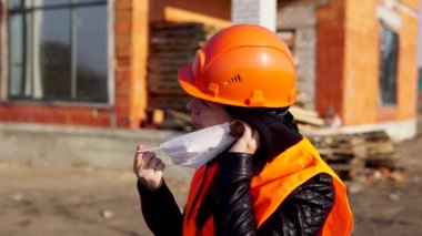 Female engineer in the construction helmet and wearing protective mask inspects a building or object reconstruction. 