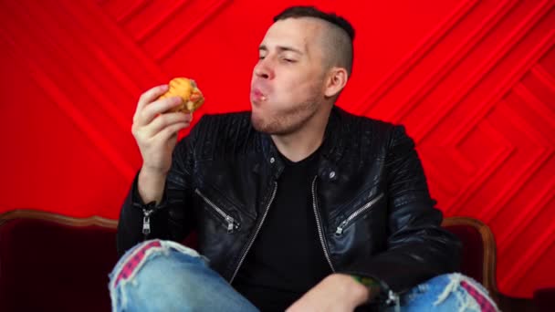 Przystojny Młody Człowiek Jedzący Hamburgera Spoczywającego Małej Sofie Pod Czerwoną — Wideo stockowe