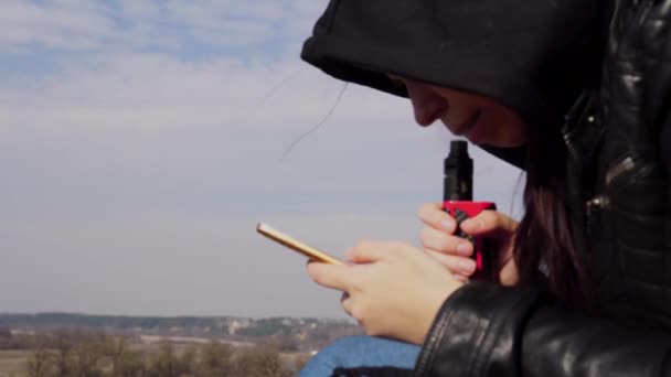 Nowoczesna Dziewczyna Pali Vape Używa Telefonu Modne Nowe Urządzenie Wapnowania — Wideo stockowe