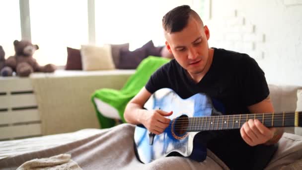 Göğsünde Dövme Olan Genç Bir Adam Yatak Odasında Gitar Çalar — Stok video