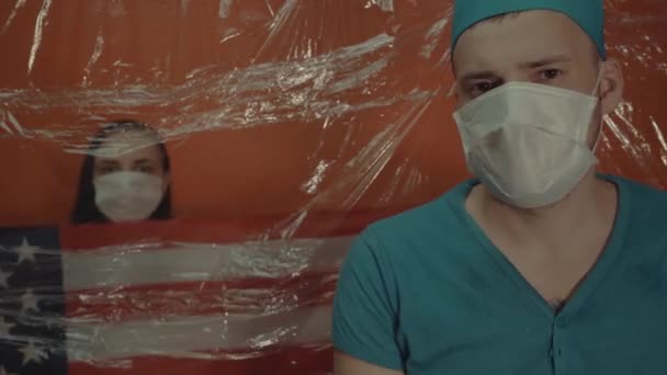 戴着医疗面罩的年轻女子 戴着美国国旗 被迫与结肠炎病毒隔离 戴口罩的男医生在前景中隔离了与病毒传播有关的病人 — 图库视频影像