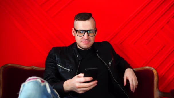 Stilig Ung Man Med Glasögon Vilar Med Smartphone Liten Soffa — Stockvideo