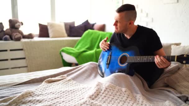 Göğsünde Dövme Olan Genç Bir Adam Yatak Odasında Gitar Çalar — Stok video