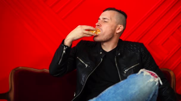Ein Hübscher Junger Mann Isst Burger Auf Einem Kleinen Sofa — Stockvideo