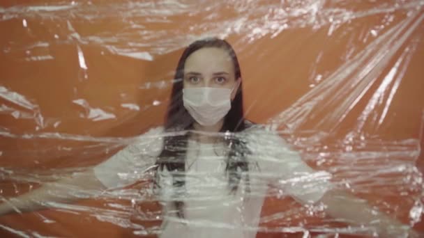 オレンジ色の背景にコロノウイルスから隔離されたアメリカ国旗を持つ医療用マスクの若い女性 病気から身を守るために仮面で顔を覆う女性の肖像画 流行の概念 — ストック動画