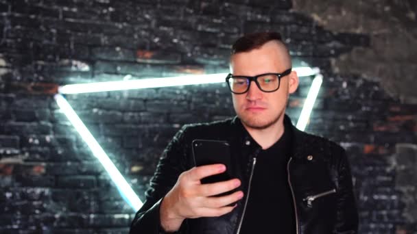 Jonge Man Met Bril Bladert Door Nieuws Mobiele Telefoon Achtergrond — Stockvideo