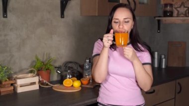 Genç çekici kadın mutfakta portakal suyu içiyor. Çekici bir kadının portresi. Geceleri ferahlatıcı bir içki içiyor..