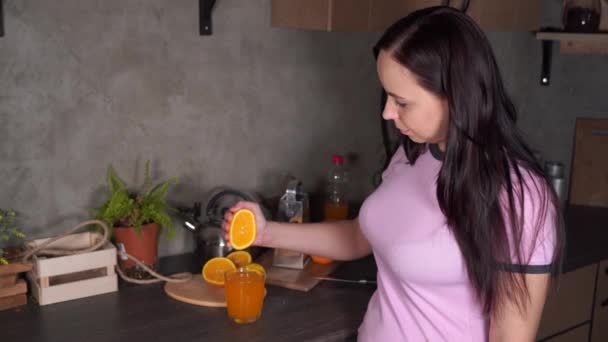 一个女孩在厨房挤压一个橙子 以获得新鲜榨橙汁 女人挤橙汁 切橙子榨新鲜果汁 有用的食物概念 — 图库视频影像