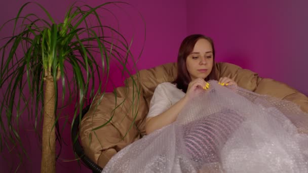 Junge Frau Spielt Mit Luftpolsterfolie Und Sitzt Sessel Zimmer Brünette — Stockvideo