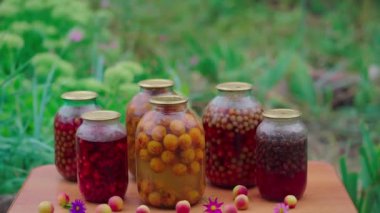 Masada kompostosu olan kavanozlar. Mühürlü cam kavanozlar ve kompot bahçedeki yaz günü çiçeklerin ve meyvelerin yanına konur.