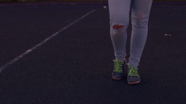 Kaldırımlı yolda delikleri ve spor ayakkabıları olan kot pantolonlu kadınların bacaklarını kapatın. Yazın şehir caddesinde duran tanınmayan kişi.