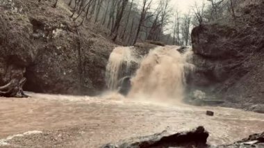 Dağlık arazide güzel, çamurlu bir şelale manzarası. Kirli dağ su yolu aşağı akıyor ve su sıçrıyor..