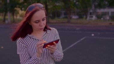 Yazın sokakta cep telefonuyla oyun oynayan genç bir kadın. Güzel bir kadın akıllı telefonuna bakıyor, caddede duruyor..