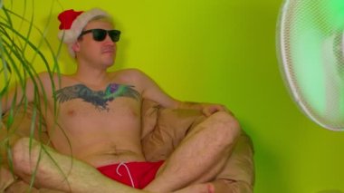 Vantilatörden önce koltukta oturan çıplak gövdeli Noel Baba şapkalı genç adam. Güneş gözlüklü yetişkin adam tatil yerindeki tatilinin tadını çıkarıyor. İzolasyon kavramı