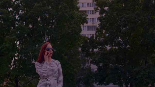 夏天的时候 戴着太阳镜 在街上拿着手机的年轻女人 站在城市街道上 用智能手机说话的漂亮女人 — 图库视频影像