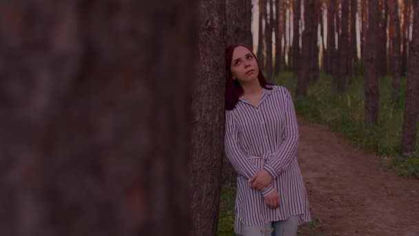 若い女性は 森の中を歩く上で木にもたれて立っている 夏に何かを考えている — ストック動画