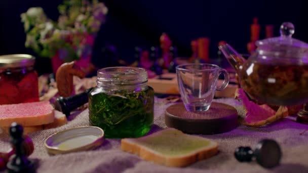 テーブルの上にジャムと空のカップを持つ小さな瓶のクローズアップ 認識できない女性がカップに緑茶を注ぐ 茶道の概念 — ストック動画