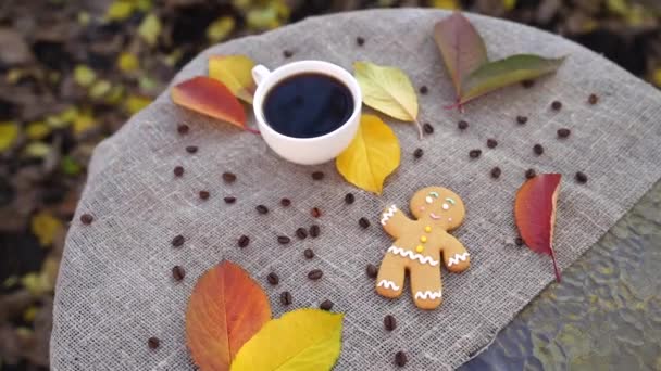 俯瞰芬芳的姜饼人和一杯浓郁的浓缩咖啡 放在色彩艳丽的秋叶旁边 桌上铺着亚麻布 停在公园里 — 图库视频影像