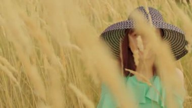 Buğday tarlasında oturan giysili ve şapkalı genç bir kadın. Güzel bayan saklanıyor, buğday başağında oturuyor..
