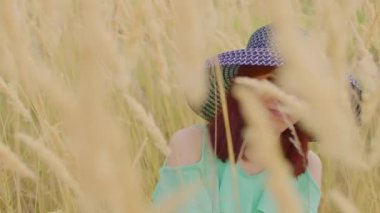 Buğday tarlasında dikilen giysili ve şapkalı genç bir kadın. Güzel bayan buğday başağında duruyor..