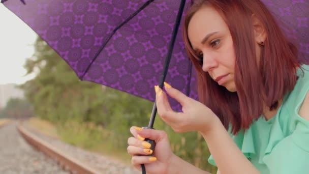 Молода Жінка Парасолькою Натирає Очі Сидячи Залізниці Похмуру Вітряну Погоду — стокове відео