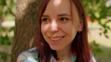 Park alanındaki ağacın yanında oturan genç bir kadın dinleniyor. Esmerin portresi, düşünceli bir şekilde başka yöne bakıyor ve yazın parktaki ağacın yanında oturuyor..