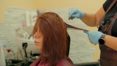 Tanımlanamayan kişi kuaförde genç bir kadının saçını boyuyor. Eldivenli bilinmeyen kuaför. Güzellik salonunda müşterinin saçını boyuyor. Bakım ve güzellik kavramı