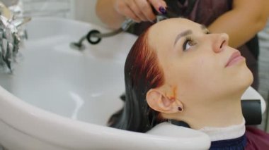 Genç bir kadın kuaförde saç bakımı sırasında başını lavaboya sokuyor. Güzellik salonunu boyadıktan sonra müşterinin saçını yıkayan tanınmamış biri. Bakım ve güzellik kavramı.