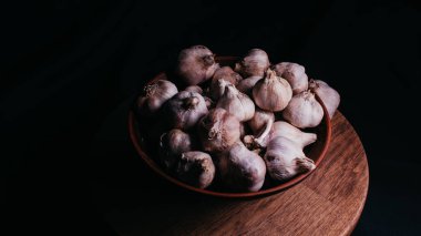 Masadaki seramik kasede bir tomar sarımsak. Siyah arka planda soyulmamış sebze hasadı