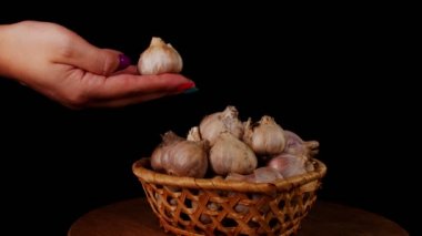 Hasır sepetin içinde, masanın üstünde bir tomar sarımsak. Kadının eli sarımsağı hasır sepete koyar.