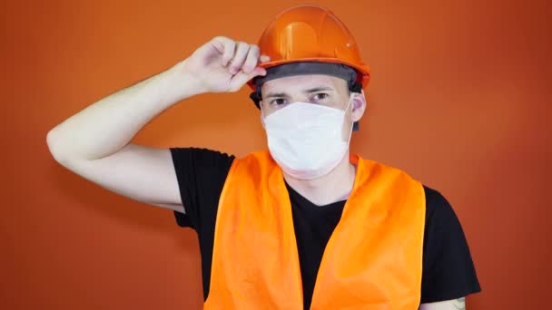 Портрет молодого человека в медицинской маске на его лице на оранжевом фоне. Взрослый мужчина покрыл лицо маской, чтобы защитить себя от болезней. Концепция коронавирусной эпидемии или болезней . — стоковое видео