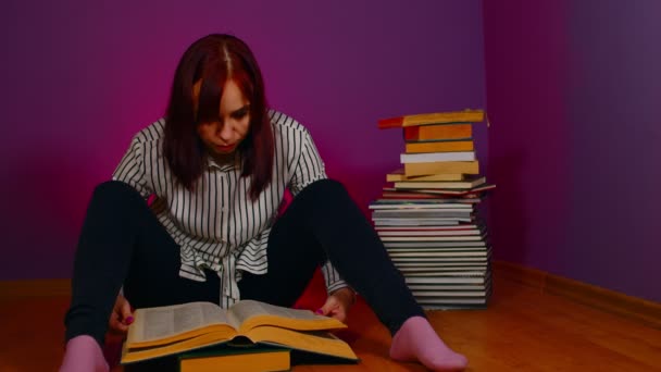 年轻女人坐在地板上 手里拿着一堆书 翻阅着紫色背景的书 穷困潦倒的学生晚上看书 准备上教育课 — 图库视频影像