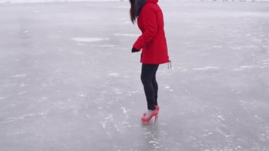 Kışlık giysiler ve yüksek topuklu ayakkabılar giyen genç bir kadın buzda süzülüyor. Kışın buz pateni pistinde çılgın bir kadın..