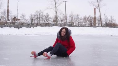 Kış kıyafetleri ve yüksek topuklu ayakkabılar giyen genç bir kadın sonbahardan sonra buzda oturur. Kışın buz pateni pistinde sürünen çılgın bir kadın.