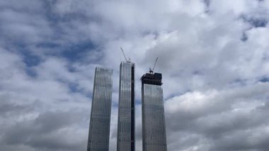 Vinçle inşa edilmiş modern bir bina. Bulutlu bir günde yüksek vinçle inşa edilen binanın altından. Konsept: Gökdelen inşaatı