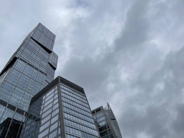Camdan duvarları olan modern gökdelen cephesi. Şehir merkezindeki bulutlu gökyüzüne karşı cam duvarları olan çağdaş yüksek gökdelenden.