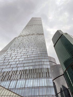 Camdan duvarları olan modern gökdelen cephesi. Şehir merkezindeki bulutlu gökyüzüne karşı cam duvarları olan çağdaş yüksek gökdelenden.