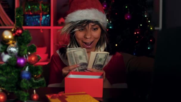 O tânără îmbrăcată într-un costum de Moș Crăciun numără bani în timp ce stă pe un scaun în fața unui computer din birou. O femeie de afaceri manager într-un costum de Anul Nou și pălărie, cu bani la locul de muncă . — Videoclip de stoc
