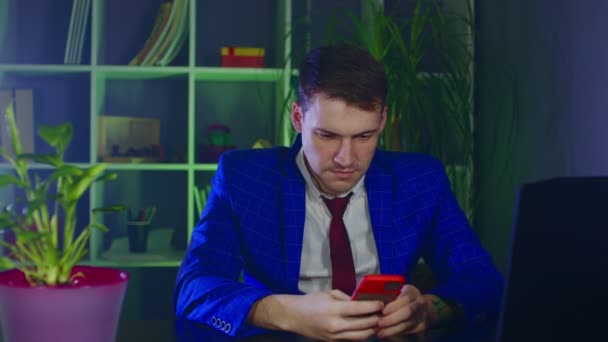 Genç adam ofiste otururken akıllı telefondan selfie çekiyor. İş adamı cep telefonuyla fotoğraf çekiyor, modern iş yerinde eğleniyor.. — Stok video