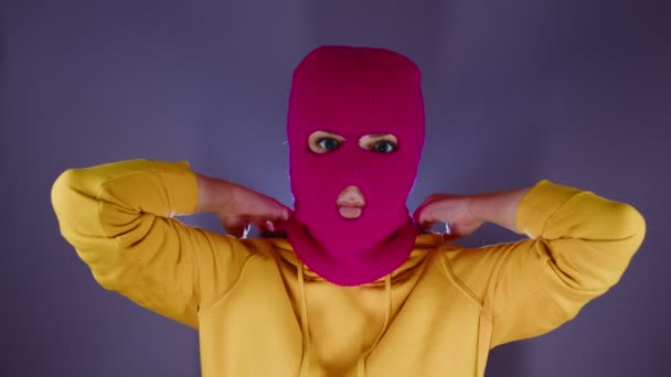 Young woman in pink balaclava puts on hood. Hooligan in mask puts on hood of hoodie, looking at camera. — Stock Video