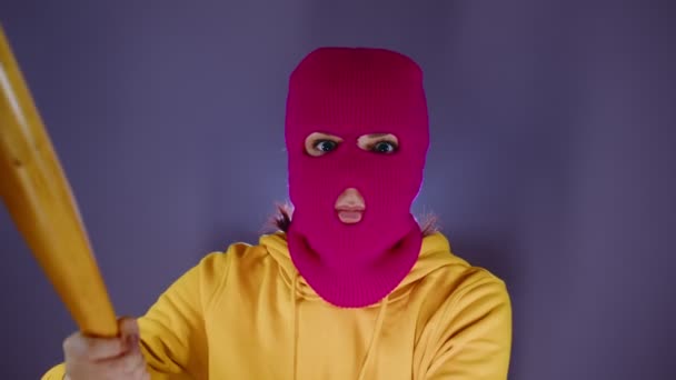 Mujer joven en pasamontañas rosa con bate de béisbol en las manos. Hooligan en la máscara late con el bate, mirando a la cámara. — Vídeos de Stock