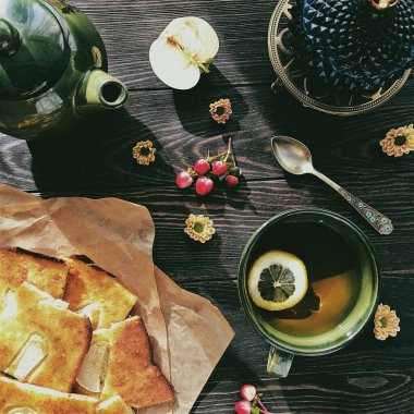 Bir çaydanlıkla hayat, limonlu bir fincan çay, ahşap bir masada turtalar ve elmalarla