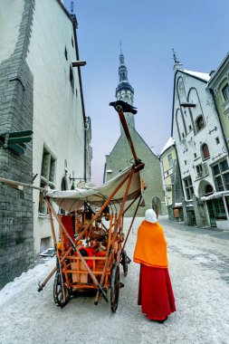 Belediye kulesine bakın. Eski Şehir 'de kış günü antika ahşap bir arabanın yanında ortaçağ geleneksel giysileri satan bir satıcıyla sokak sahnesi. Tallinn, Estonya