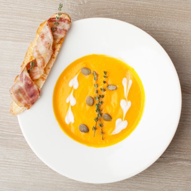 Pumpkin cream soup purée with bread slice, bacon and seeds