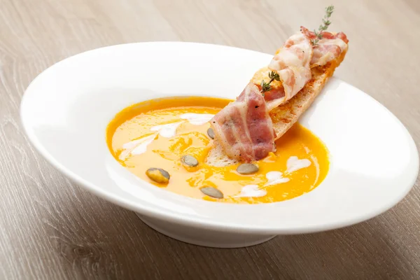 Pumpkin cream soup puree with bread slice, bacon and seeds — Stockfoto